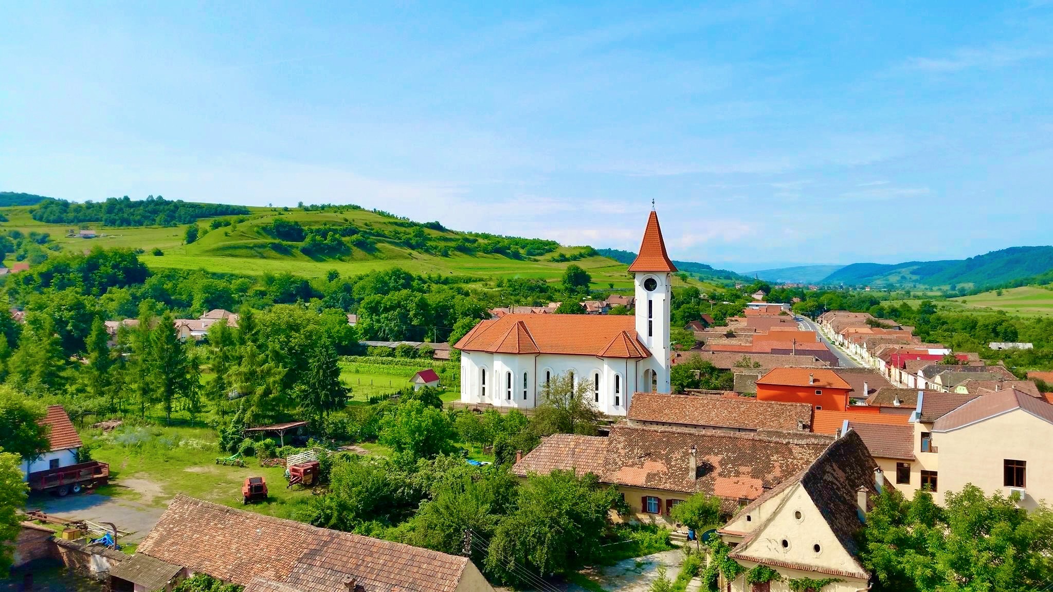 Landscape of Romanian countryside, houses line the street, lush green rolling hills frame the manmade structures.